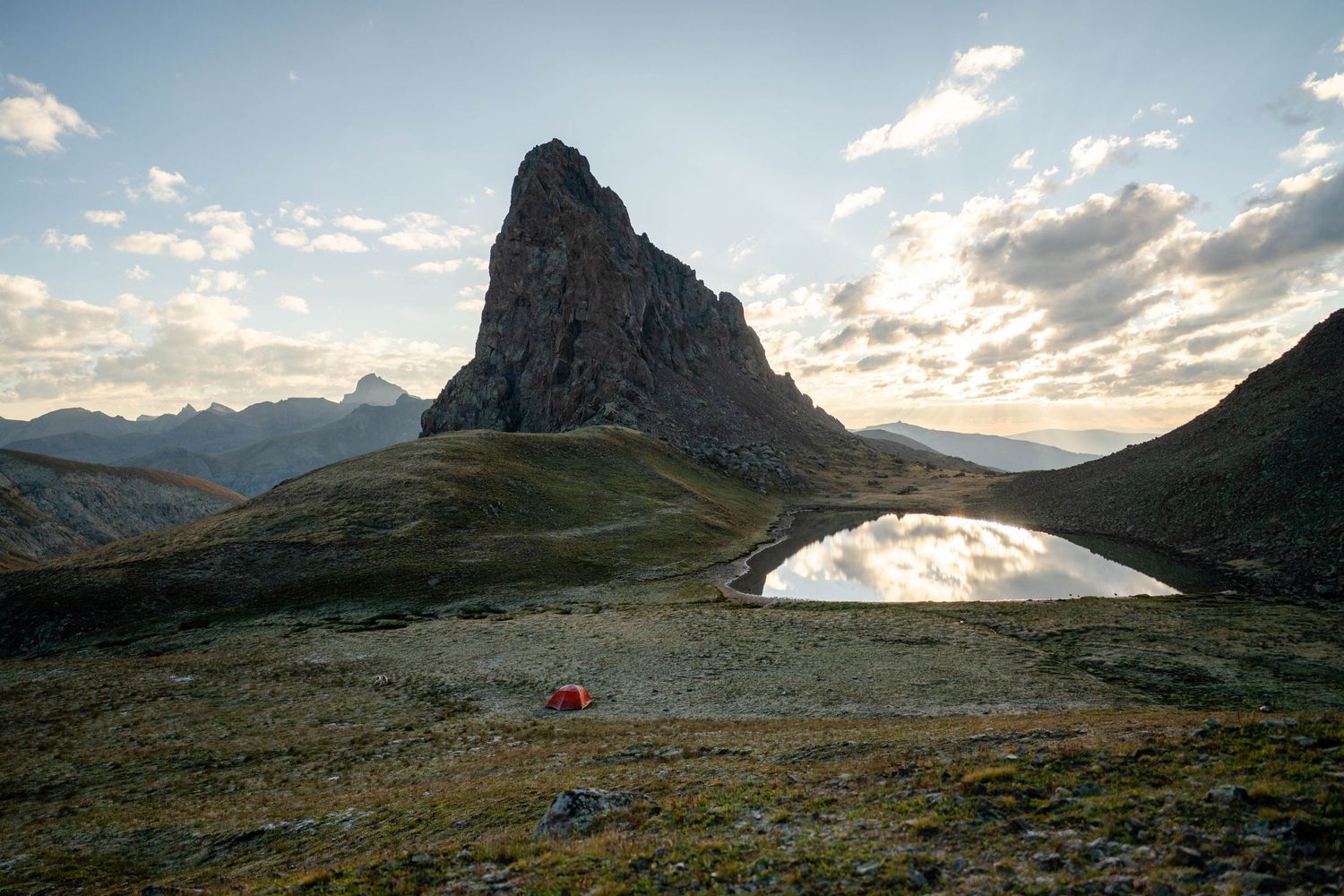 Tent set up on alpine terrain beneath a dramatic mountain peak at sunrise in the San Juan Mountains of Colorado.