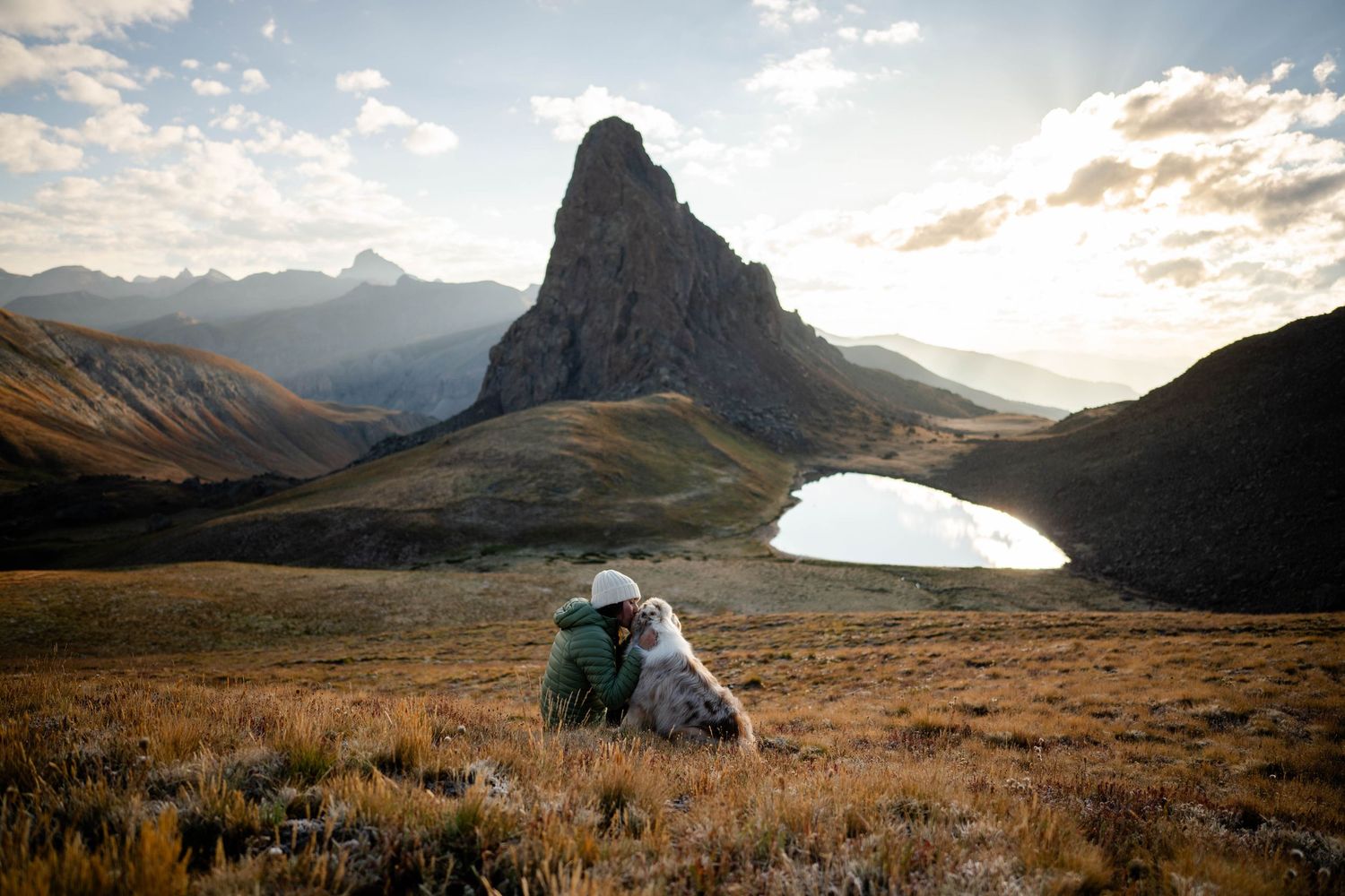 A panoramic mountain landscape at sunrise with woman and her Australian Shepherd hugging in the San Juan Mountains of Colorado