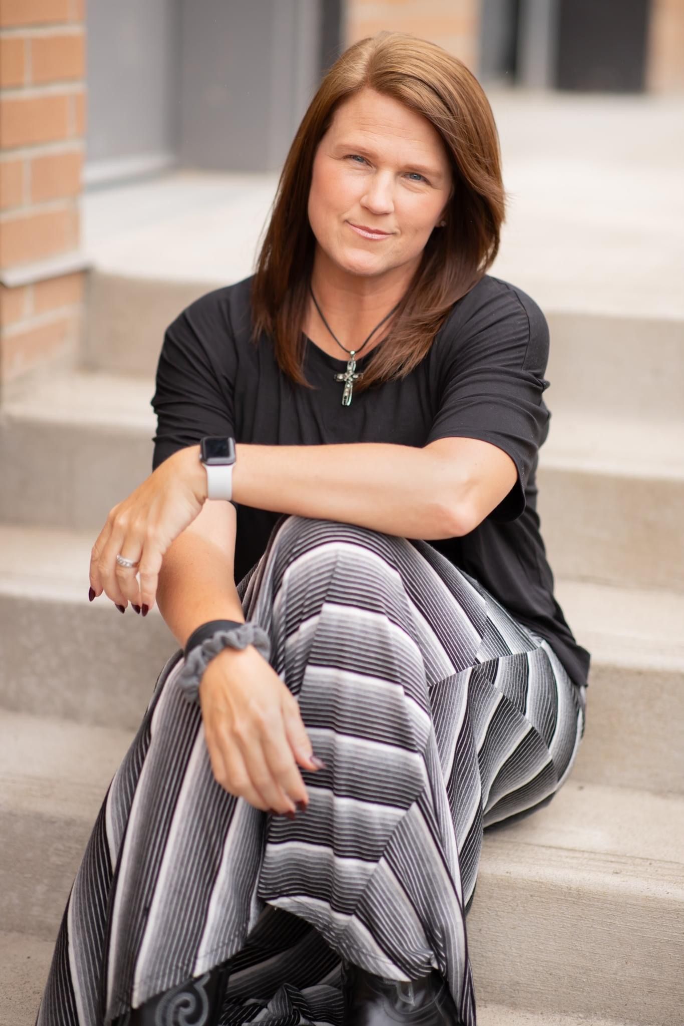 Portrait of photographer sitting on concrete steps wearing black top and striped skirt.
