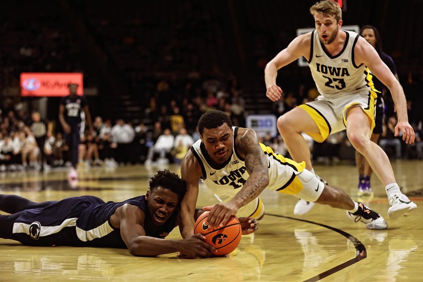 Basketball players diving for a loose ball during an intense college game.