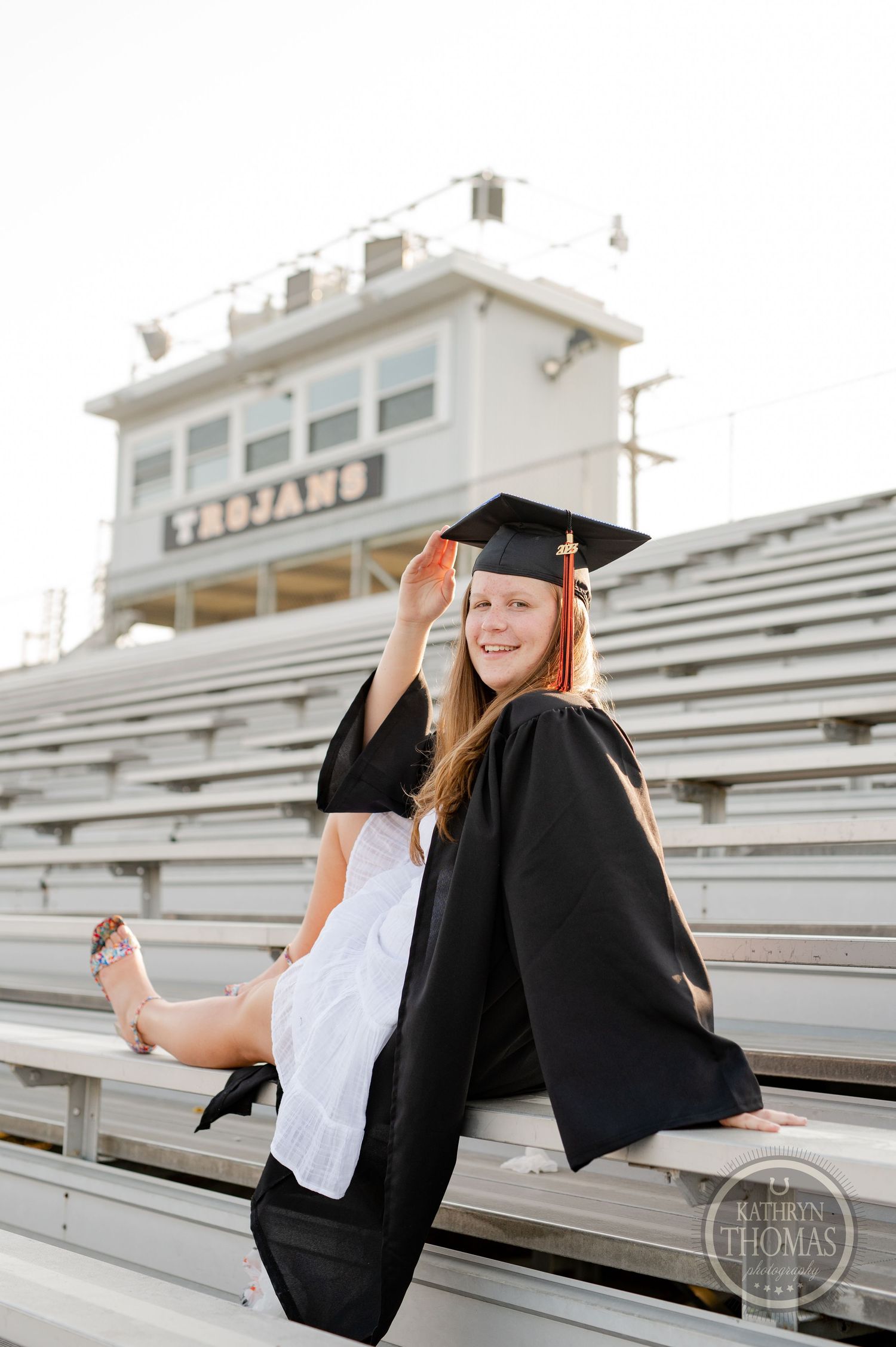 Graduate poses playfully on stadium bleachers in traditional academic regalia.