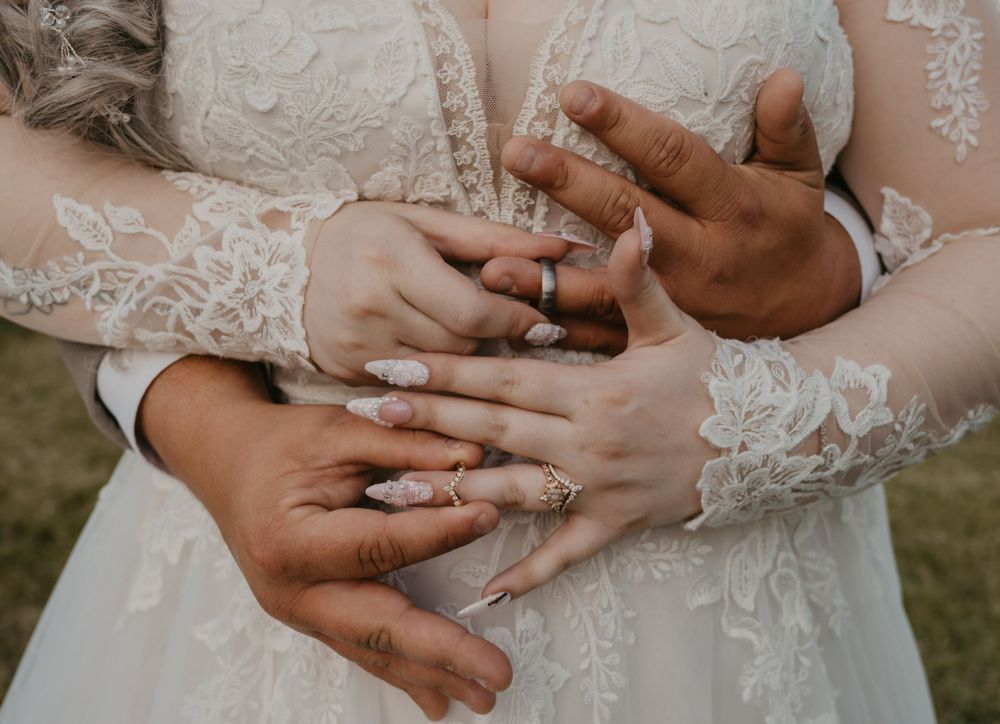 Close-up of bride and groom hands intertwined showing wedding rings, bride wearing lace gown.