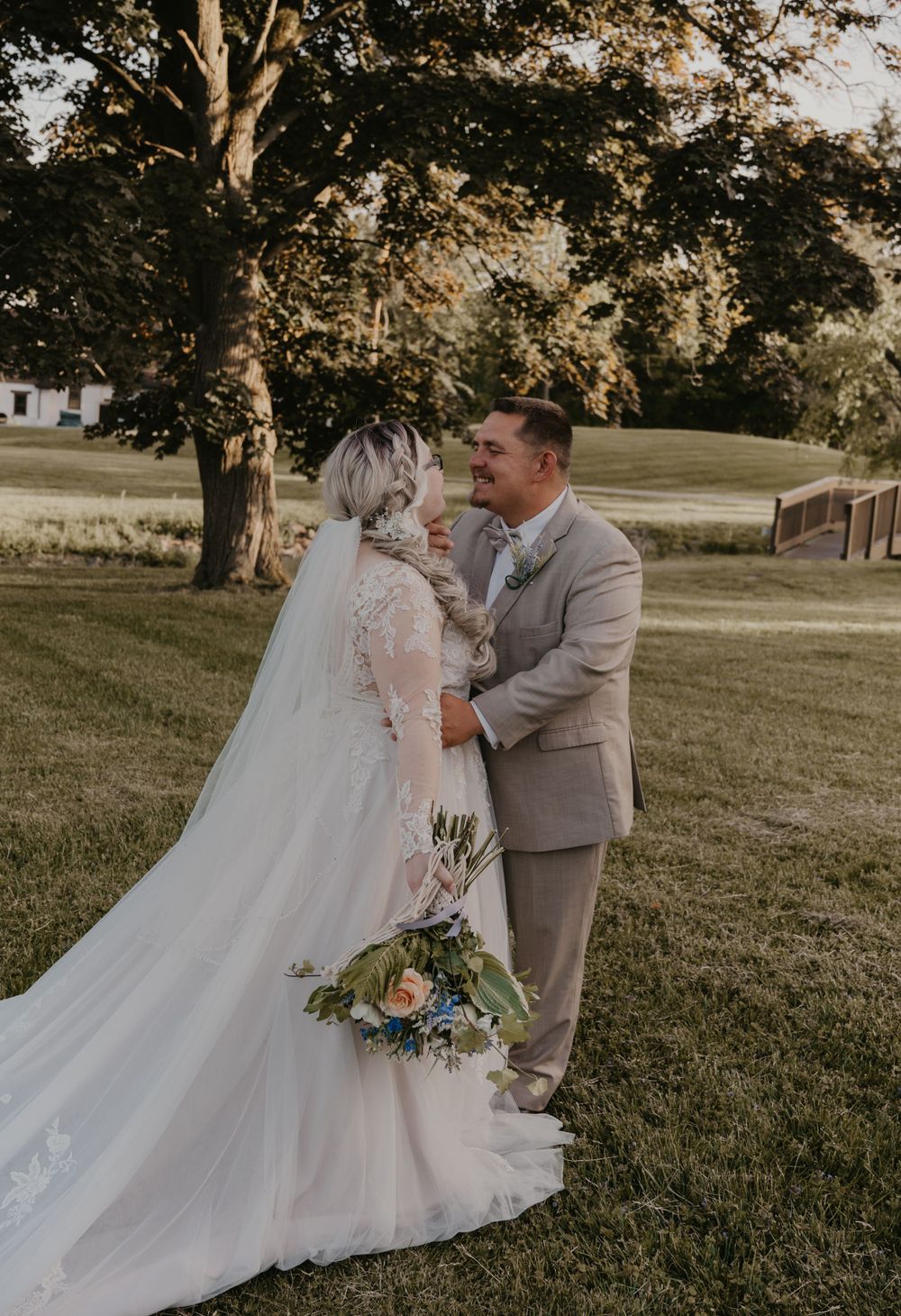 Bride and groom share a romantic moment smiling at each other in golden hour light on green lawn.