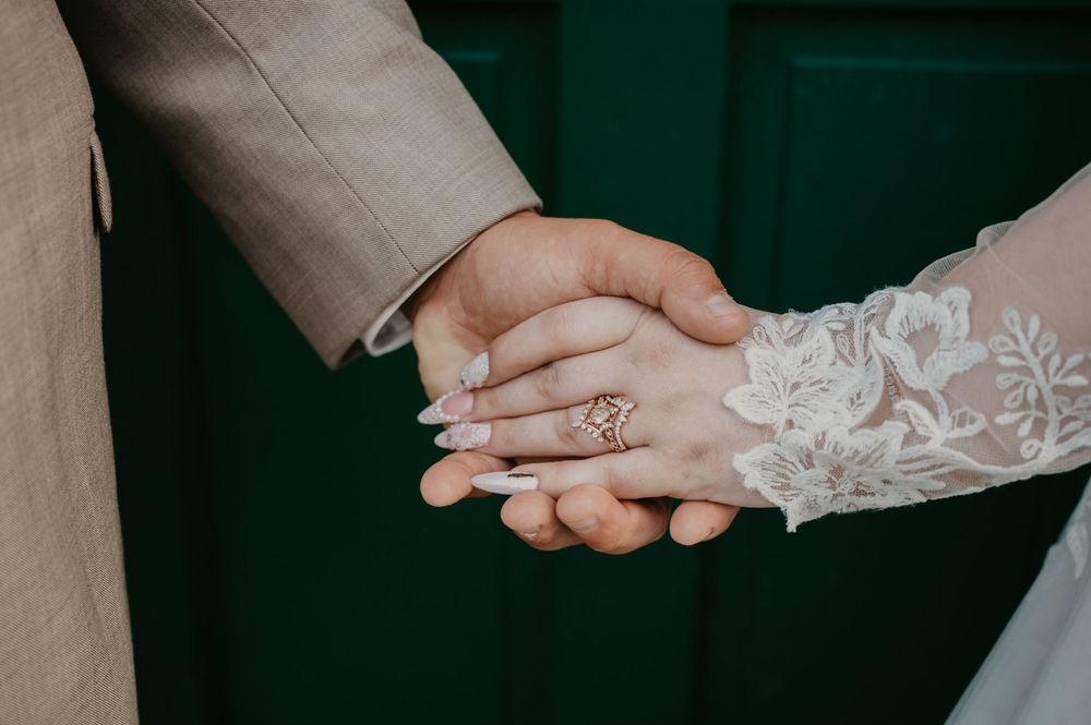 Close-up of bride and groom holding hands showing elegant engagement ring and lace wedding dress sleeve.