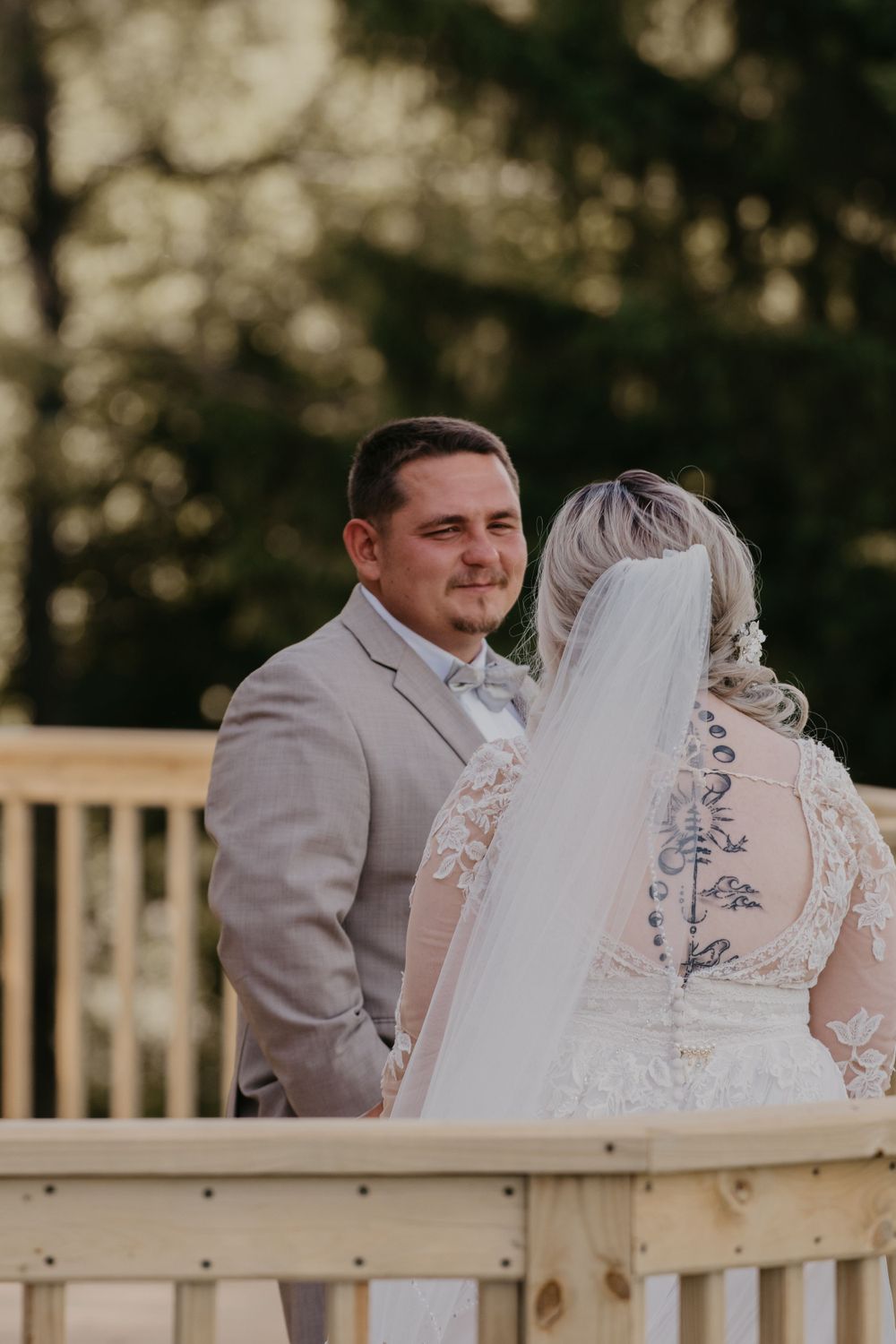 Emotional groom gazing at bride during outdoor wedding ceremony on wooden deck.