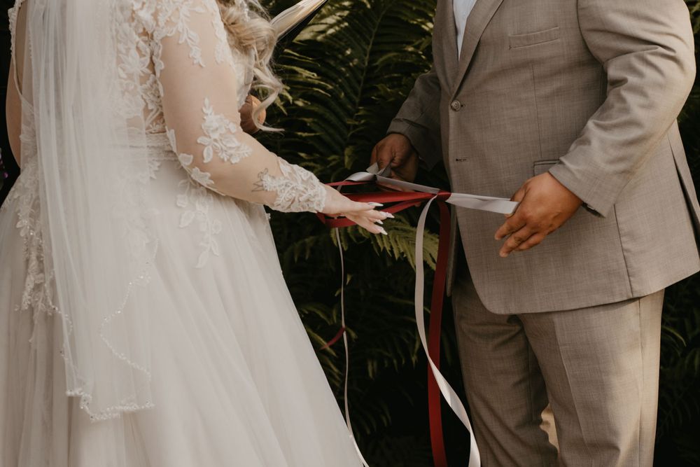 Bride and groom exchanging vows with ribbon handfasting ceremony outdoors.