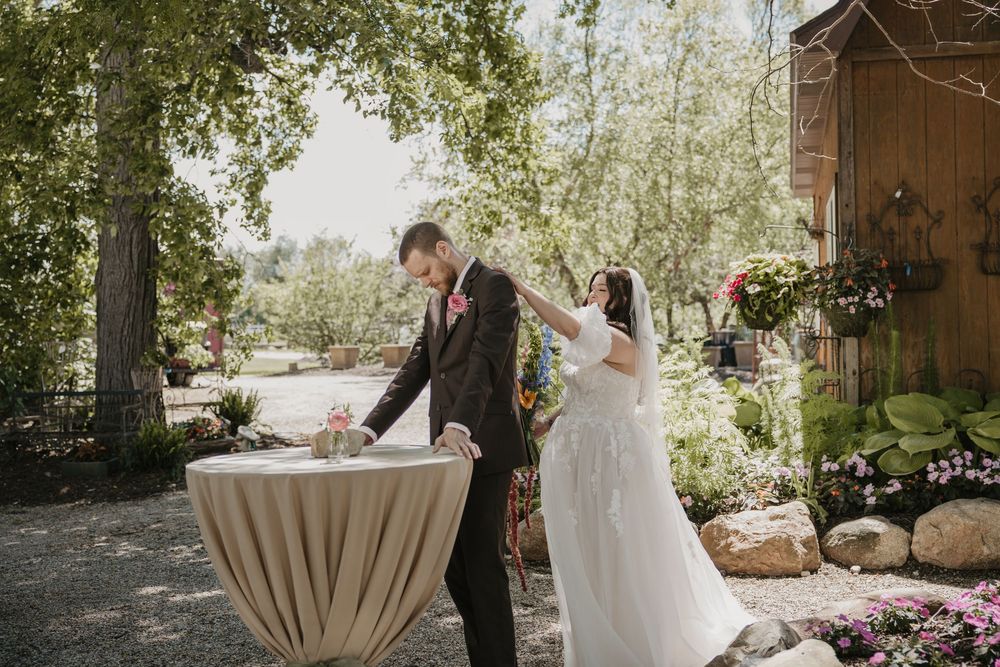 Bride and groom share a joyful moment outdoors at a garden wedding venue surrounded by lush greenery.