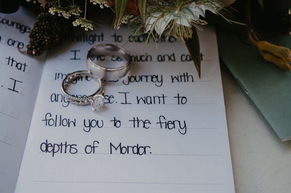 Wedding vows handwritten with Lord of the Rings Mordor reference with two wedding bands on paper.