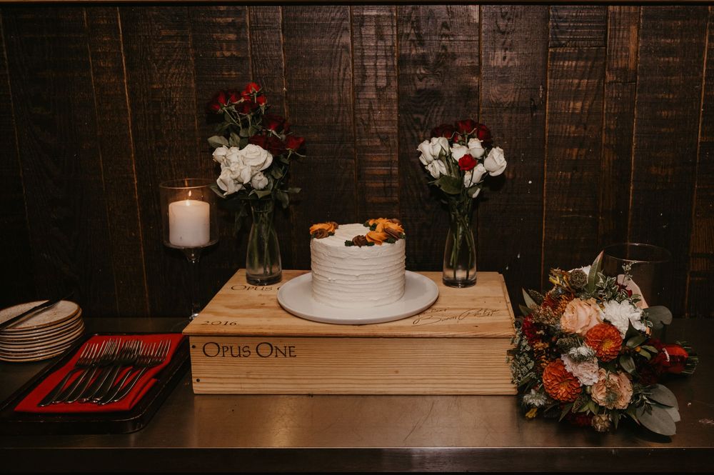 Simple white wedding cake on wine crate display with candles and floral arrangements.