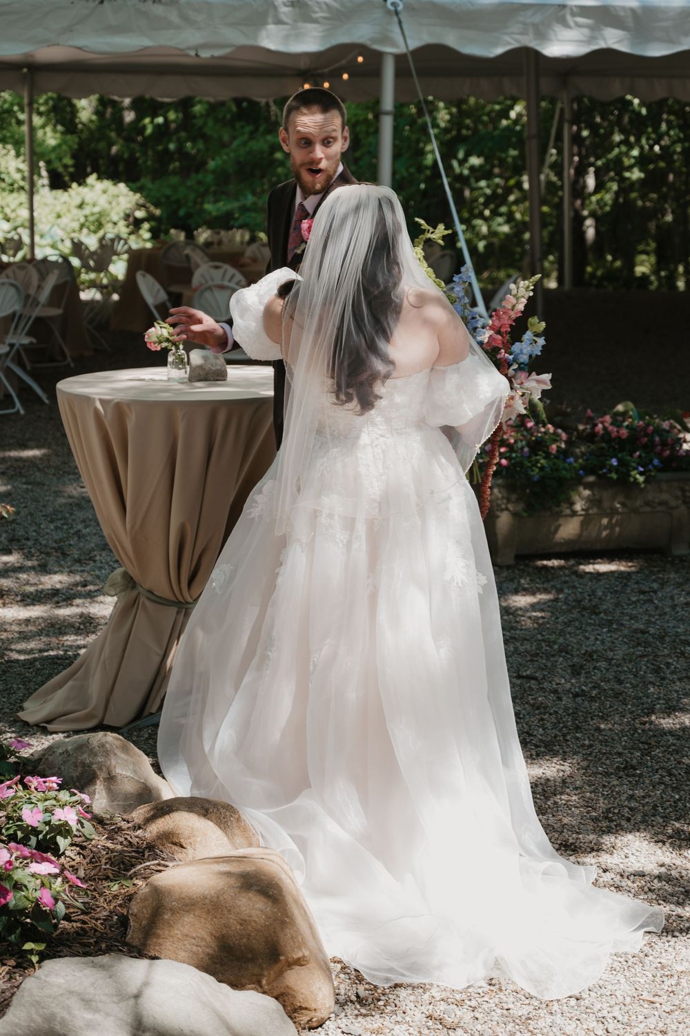 Bride in white ball gown and veil stands with groom outdoors at elegant garden wedding reception with floral decor.