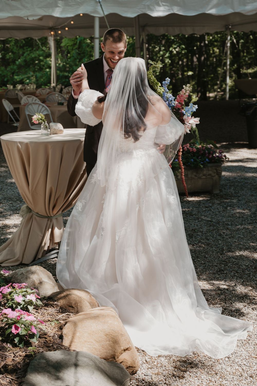 Bride and groom share a joyful dance outdoors at a garden wedding, with a dog resting near the bride's white gown train.