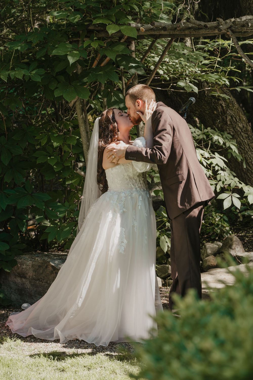 A bride and groom share a romantic kiss in a lush garden setting, with the bride wearing a flowing white gown and veil.