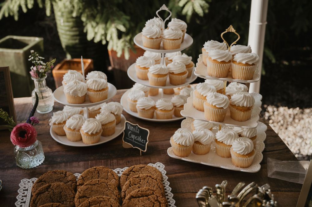 Elegant wedding dessert table with tiered cupcake stands, white frosted cupcakes, and cookies on rustic wood.