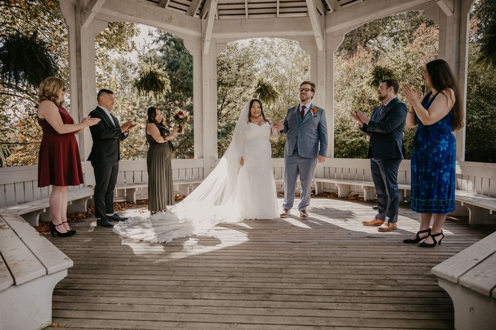 Intimate micro wedding ceremony in white gazebo with small wedding party applauding couple.