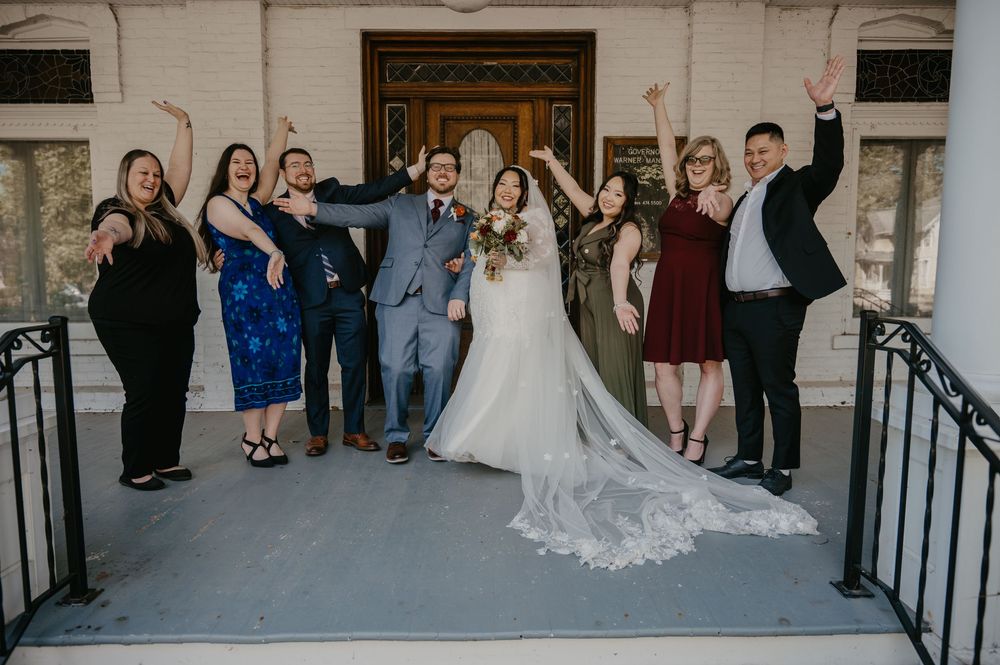 Joyful wedding party celebrating with raised arms on venue steps with bride and groom.