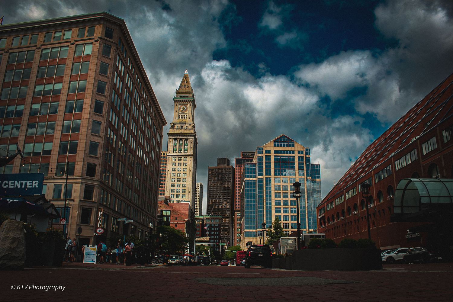 Historic Custom House Tower landmark surrounded by modern buildings under dramatic cloudy sky in Boston.
