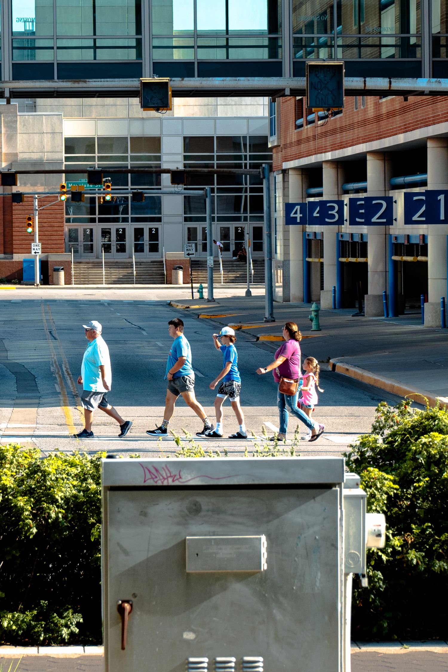 Group of four people walking across a crosswalk near a large sports stadium building.