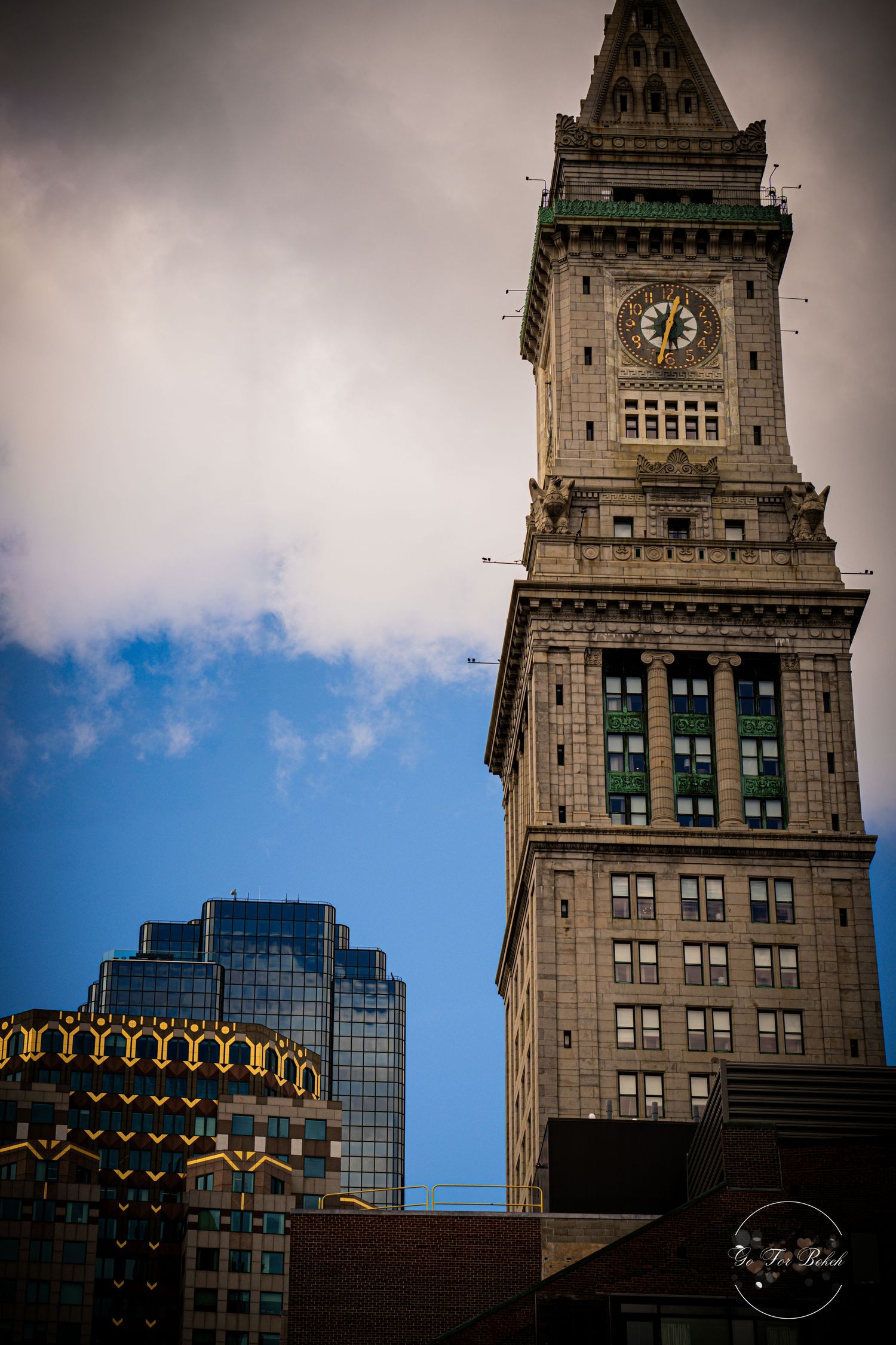 Close-up of Boston Custom House Tower clock with ornate stone architecture against blue cloudy sky.