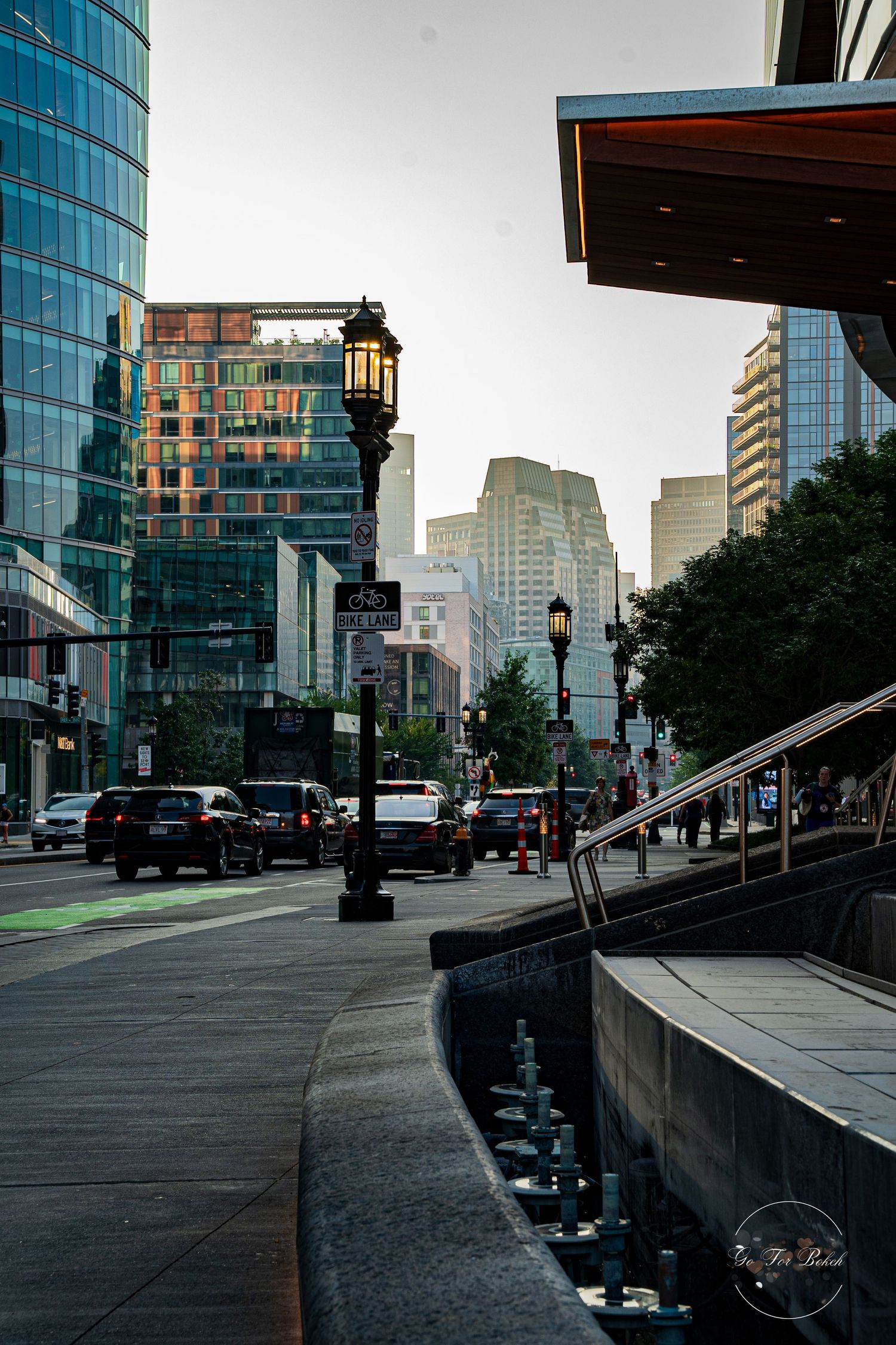 Urban street scene with vintage lamp posts, glass skyscrapers, and busy traffic at dusk in Boston.