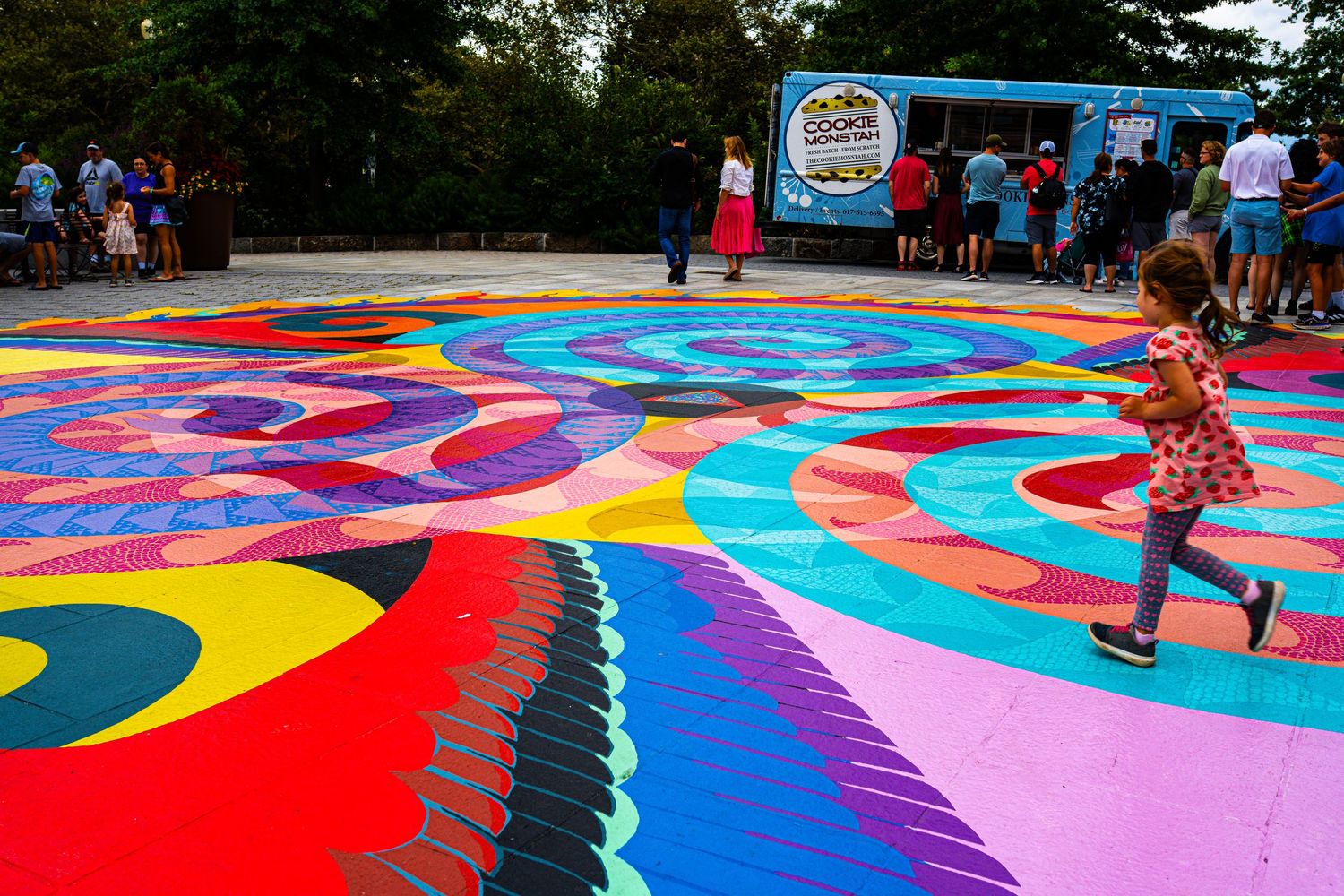 Child running across vibrant colorful mandala street art mural at outdoor community festival event.