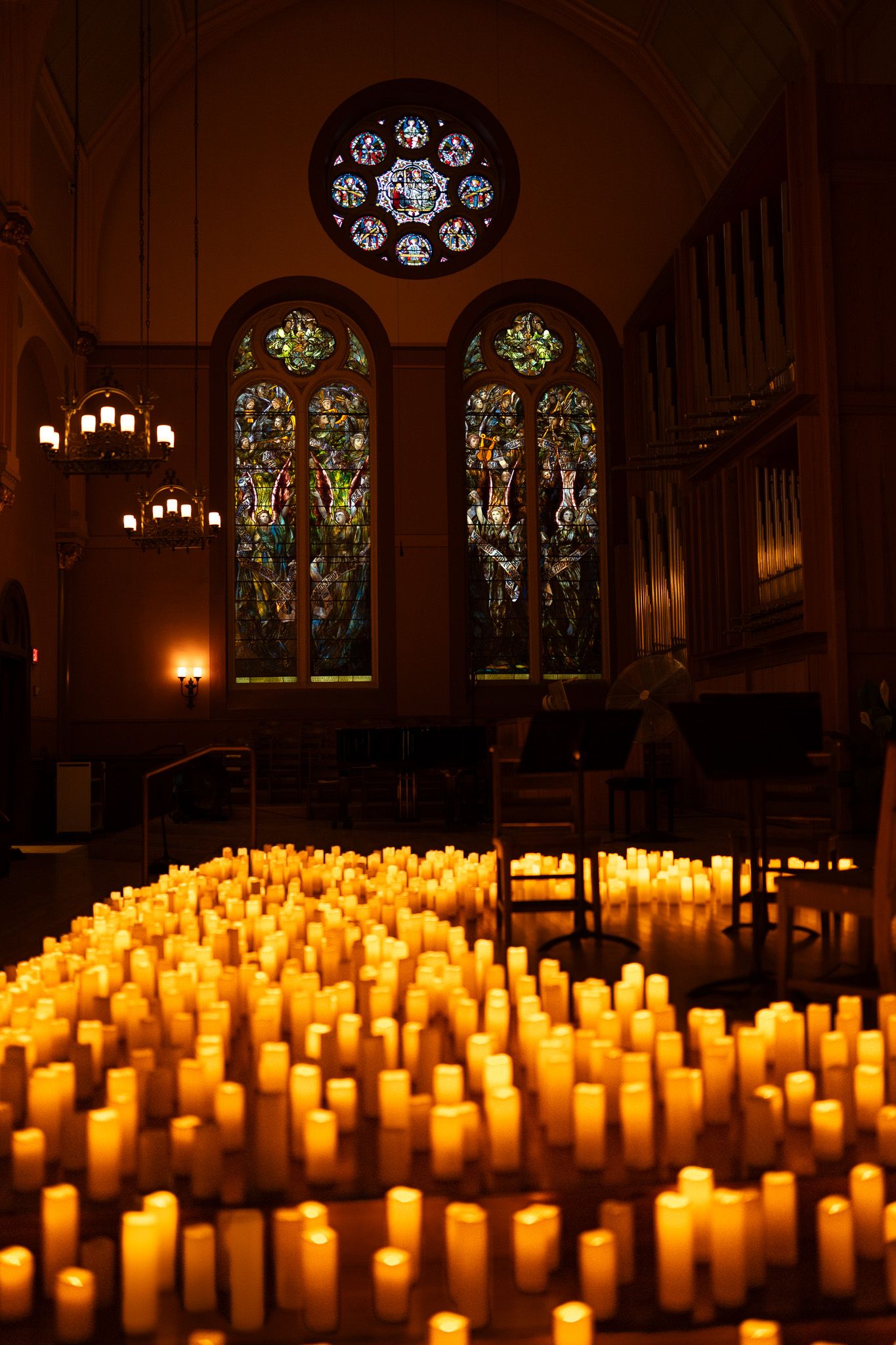 Hundreds of glowing candles arranged on a church floor before colorful stained glass windows.