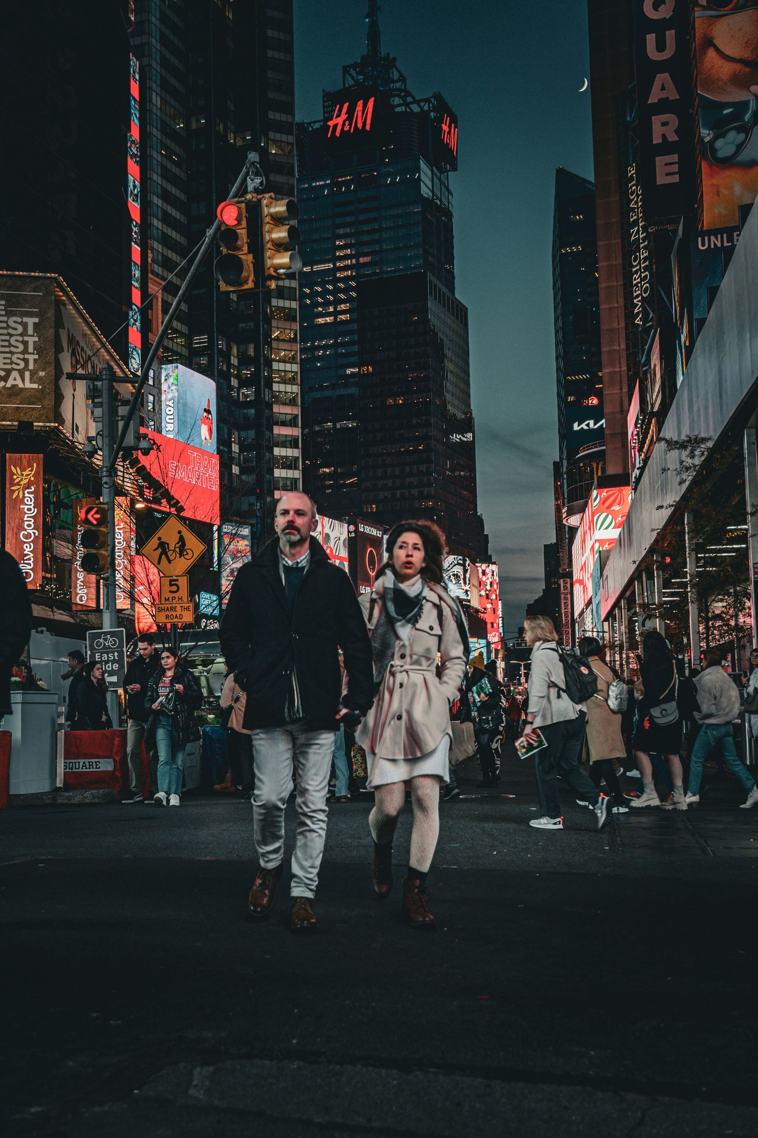 Couple walking through illuminated Times Square at night surrounded by bright neon billboards in NYC.