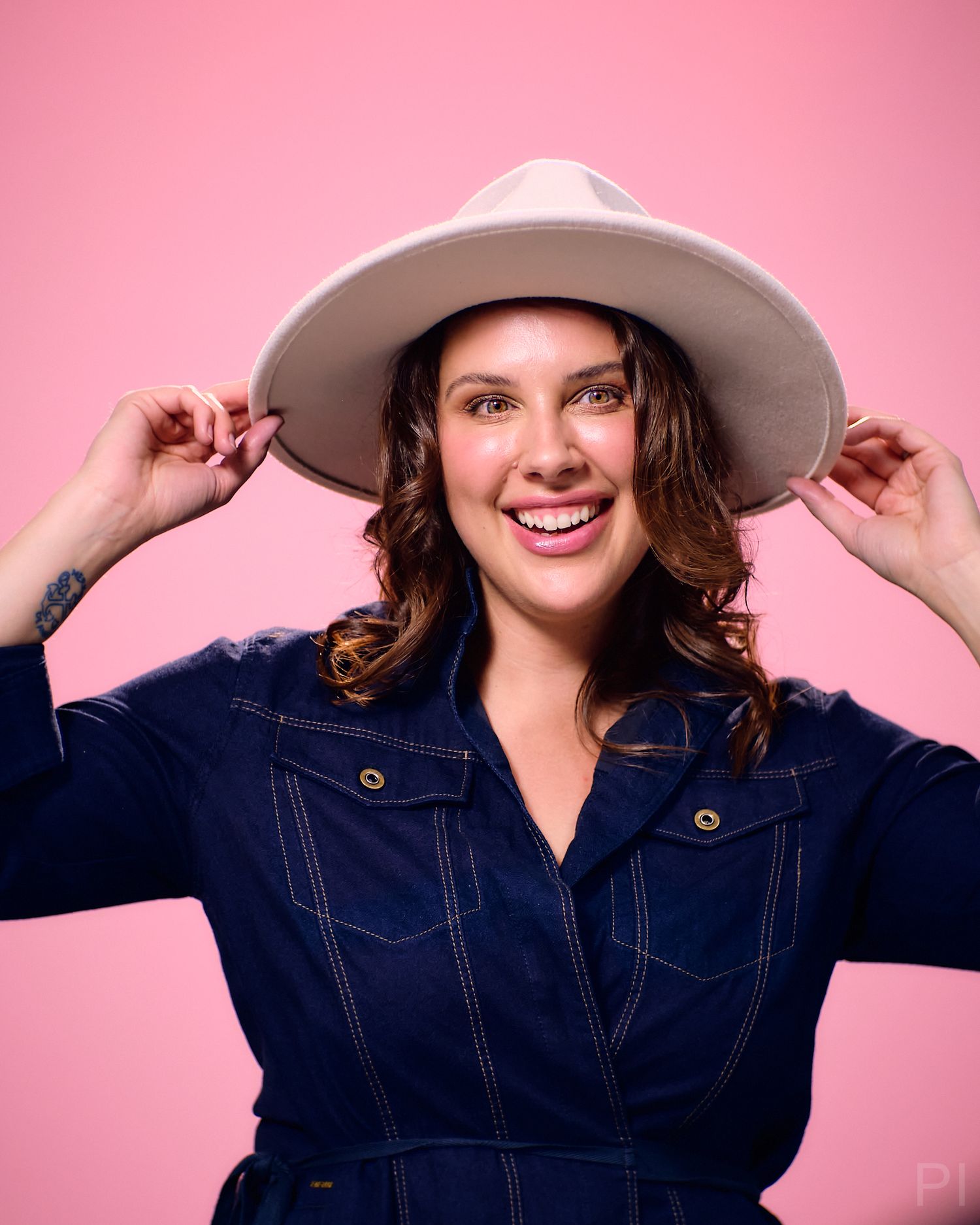 Person wearing denim outfit and wide-brimmed hat against pink background.