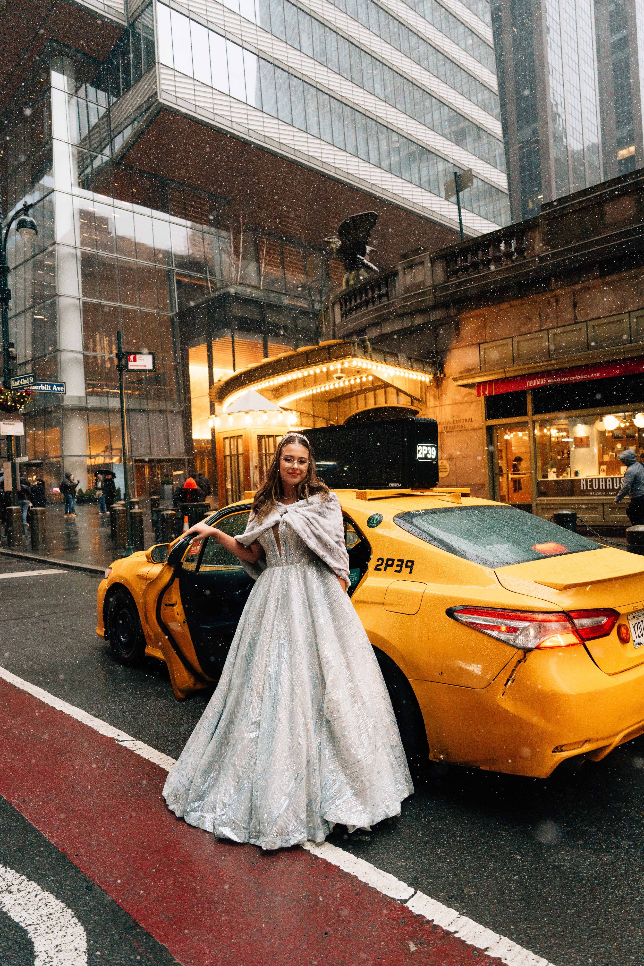 A bride in a white ballgown enters a yellow taxi cab on a rainy city street at night.