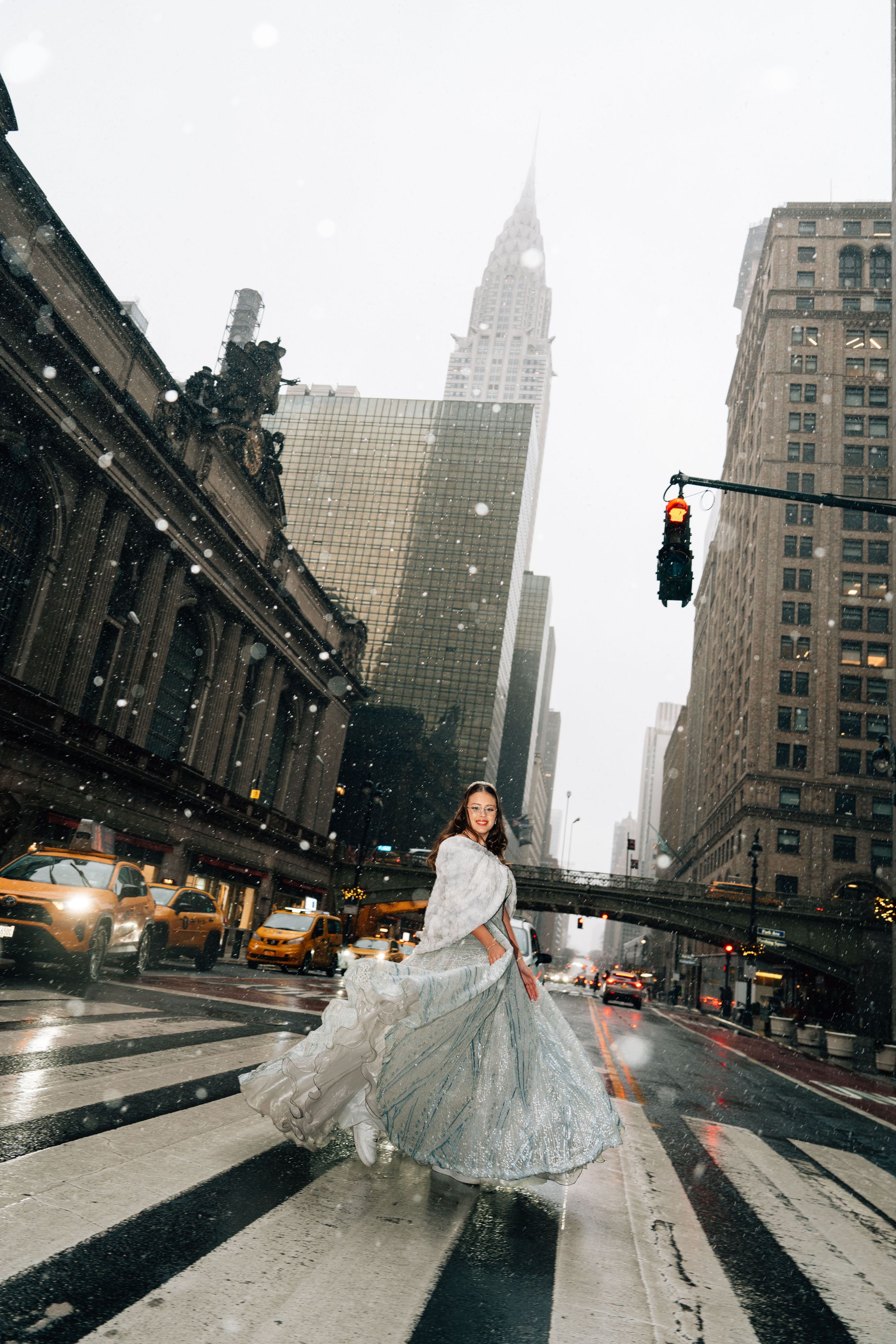 A bride in a flowing white gown poses dramatically on a snowy New York City street with skyscrapers in the background.