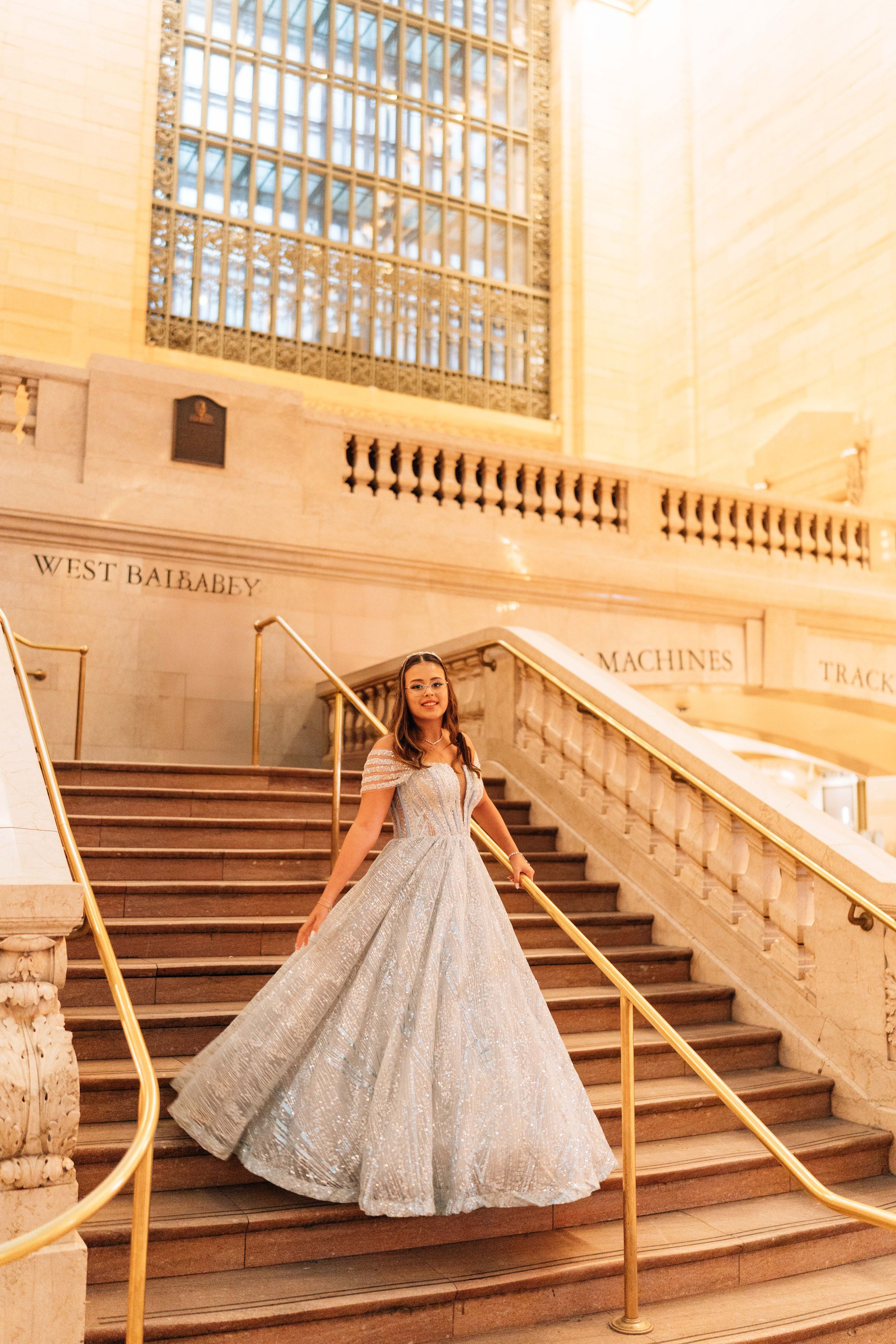 A silver sequined ball gown sparkles on the grand marble staircase of an elegant historic building.