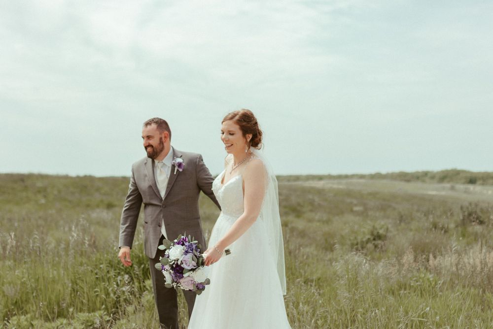 Wedding couple standing in golden grassland with overcast sky backdrop.