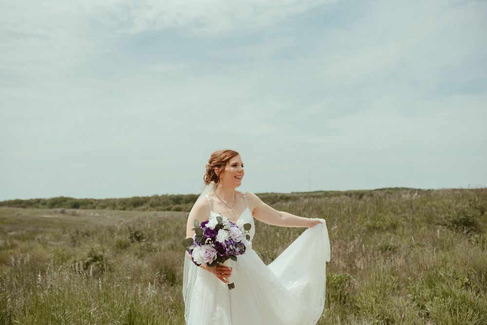 A bride in a flowing white dress holds her bouquet while standing in a grassy field.