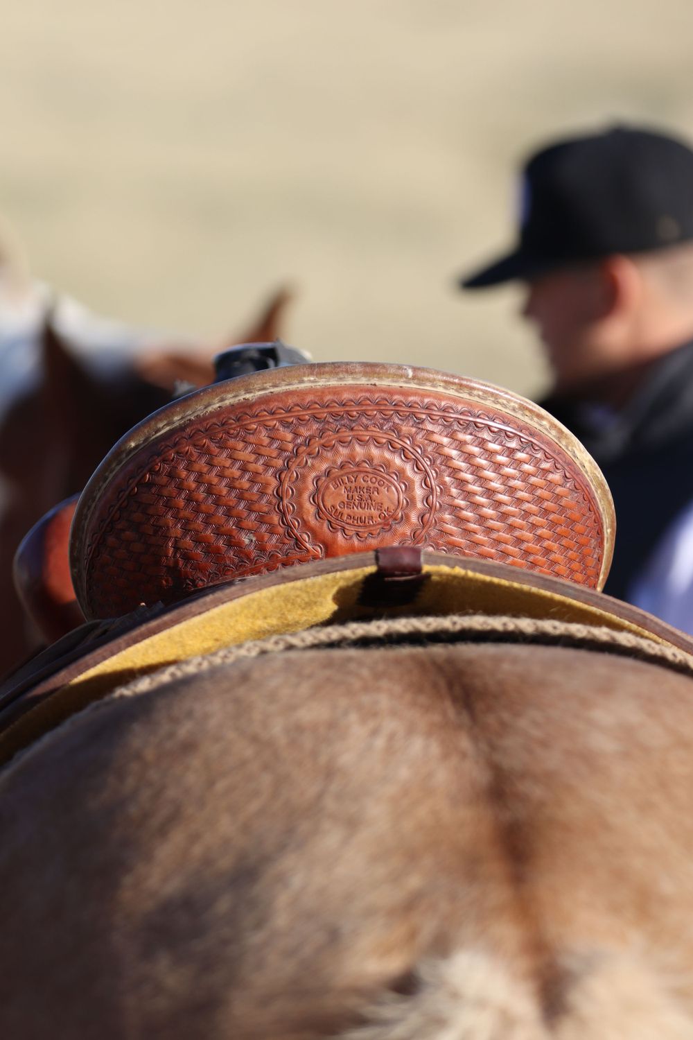 Close-up detail of a brown leather stamped western saddle on horseback.