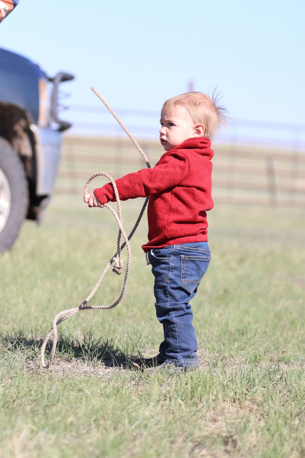 Small child in red sweater playing with a rope in a grassy field.