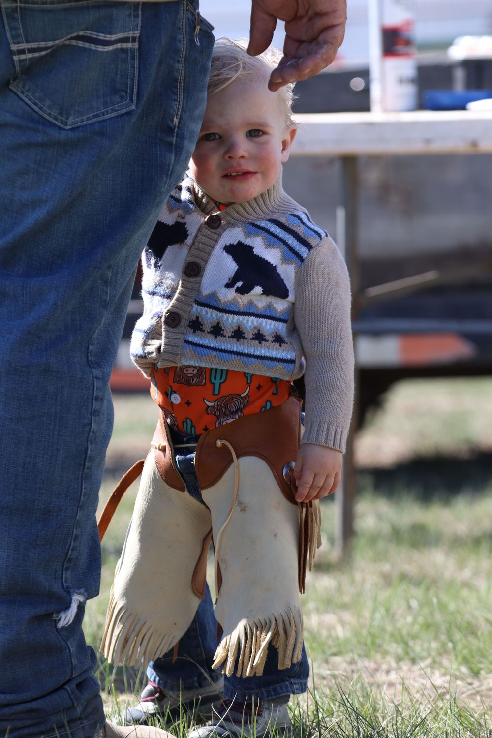 Small child wearing decorative western outfit with fringe chaps and bear sweater.