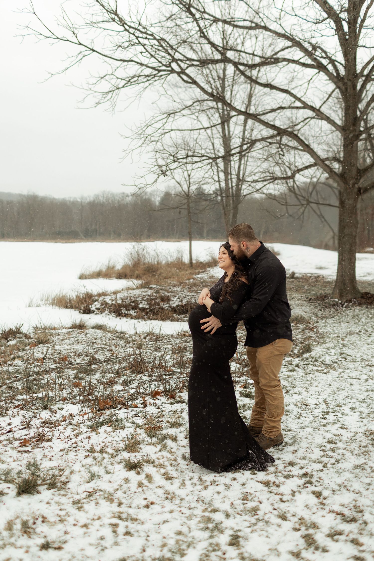 Couple embracing near water during sunset in winter landscape.