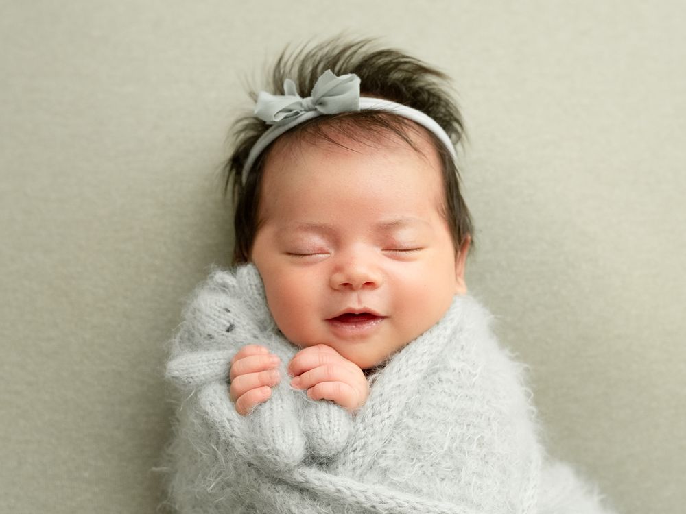 Peaceful sleeping newborn wrapped in soft gray swaddle with matching bow headband on mint background.