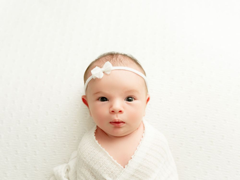Baby wearing white knit sweater and delicate lace headband against light background.