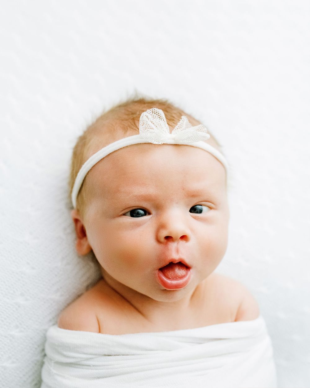 A baby wearing white shows a range of delightful expressions in a series of close-up portraits.