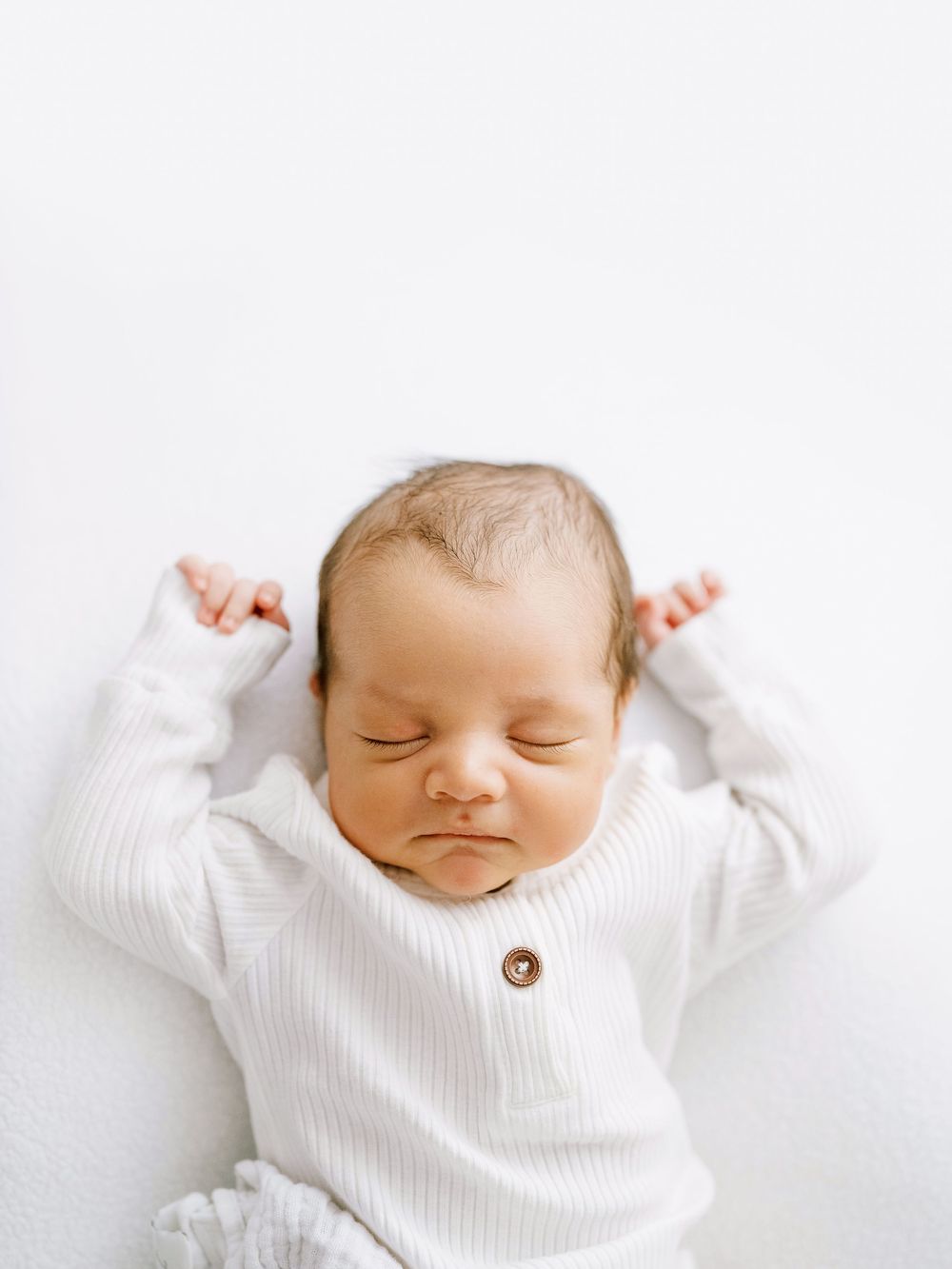 A sleeping newborn baby wearing a white knit sweater lying peacefully on a white background.