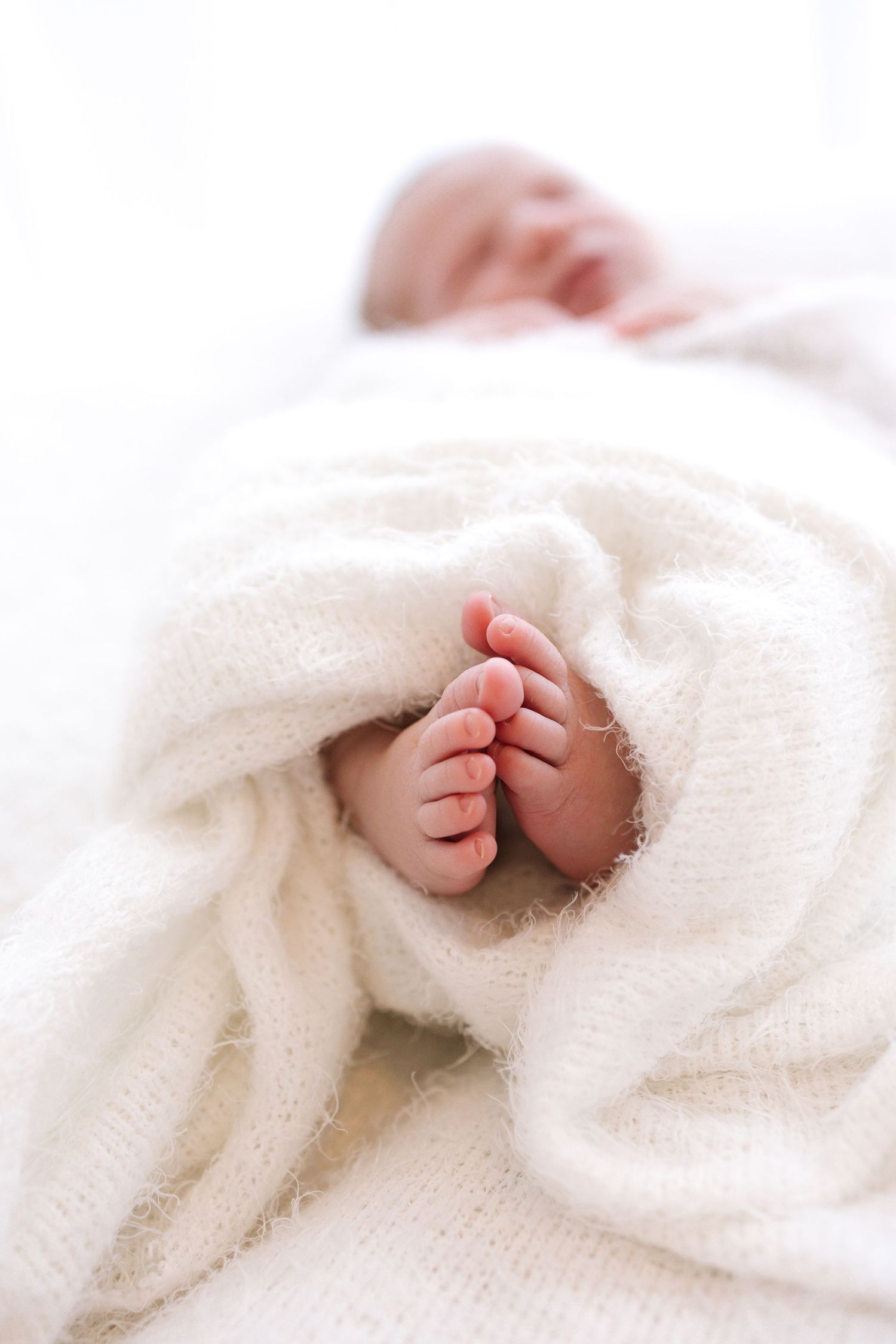 Two people lean in close to admire a sleeping newborn wrapped in white fabric.