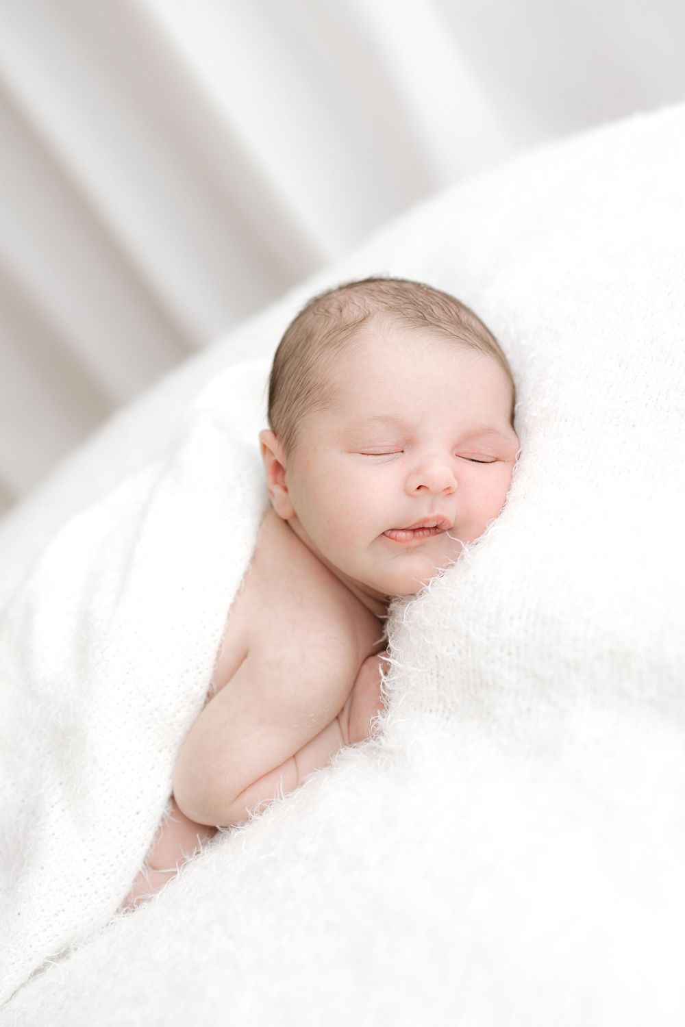 Peaceful newborn baby sleeping wrapped in a soft white fluffy blanket against a white background.