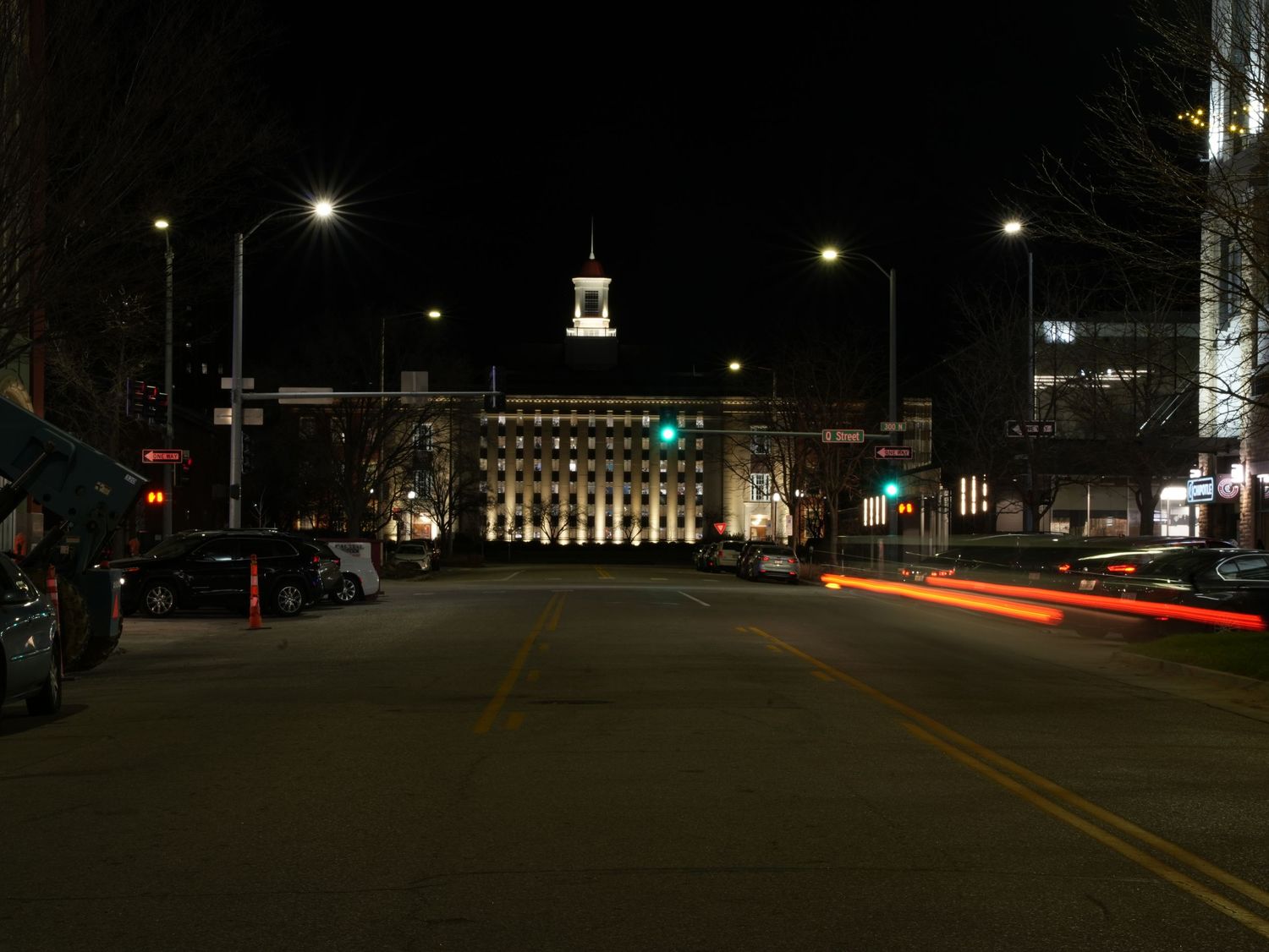A nighttime cityscape shows a historic building illuminated with street lights and traffic trails.