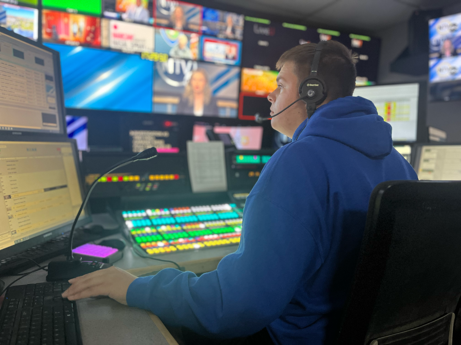 A broadcast control room operator works at a station with multiple monitors and production equipment.