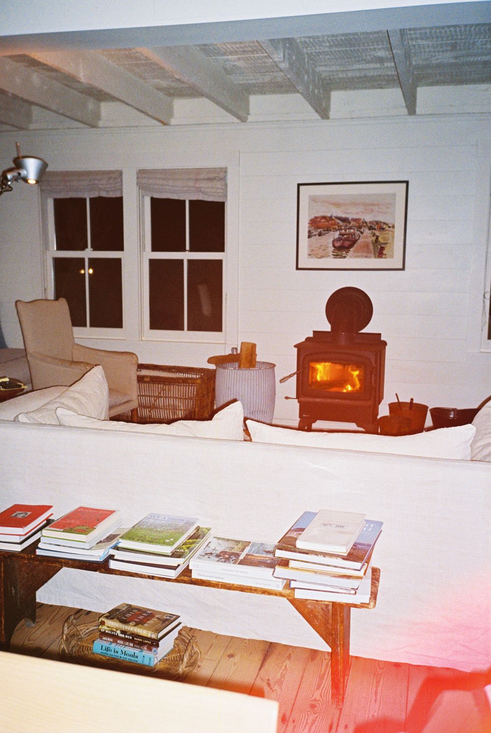Wood burning stove glowing the living room behind a couch and a bench full of artist books and cookbooks in Rockand, Maine.