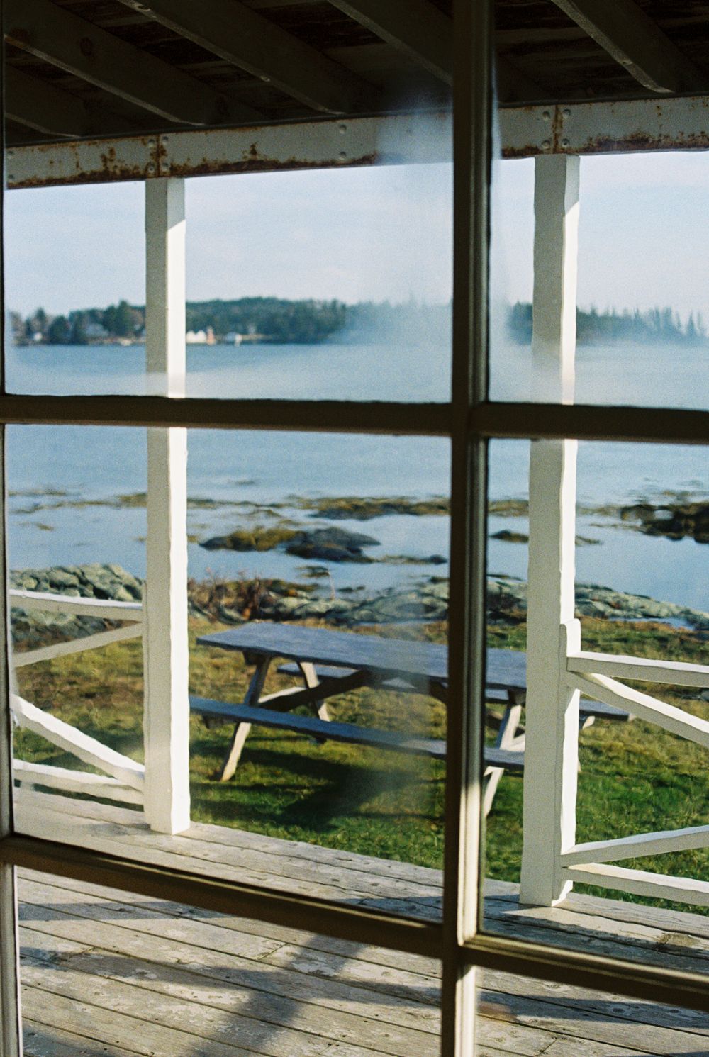 35mm photograph looking through the big glass windows out to the picnic table in front of the rising tide at Harbor Cottage.