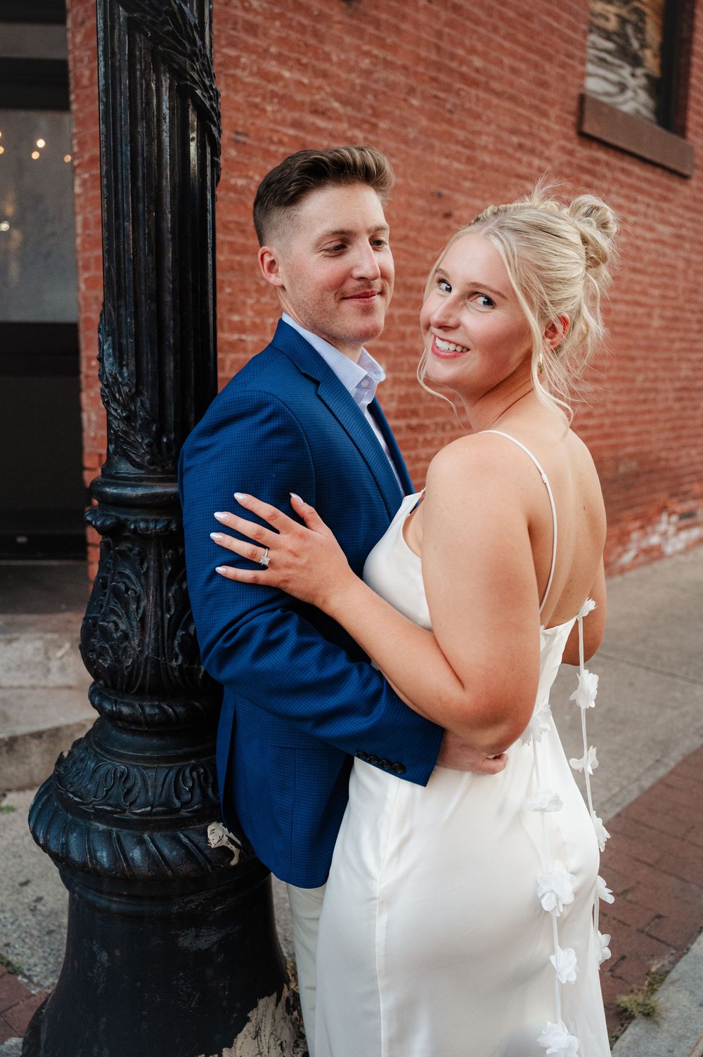 A couple shares a joyful moment together against a brick wall background during their wedding photoshoot.