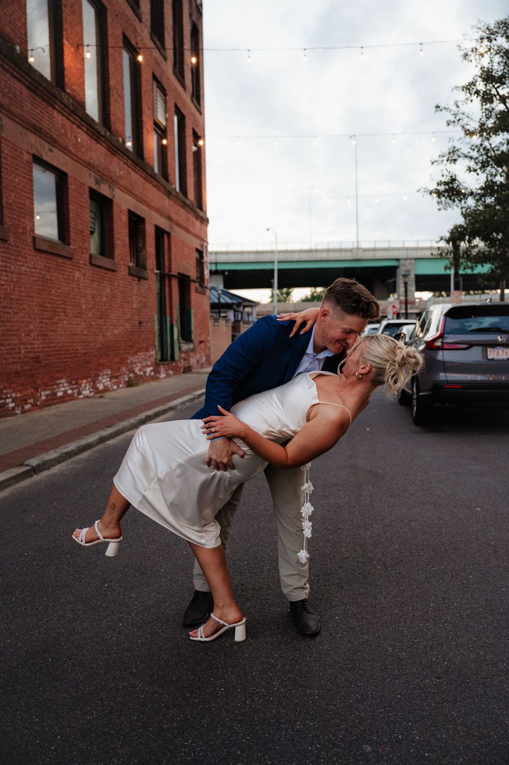 A romantic dip pose on a city street with brick buildings and an overpass in the background.