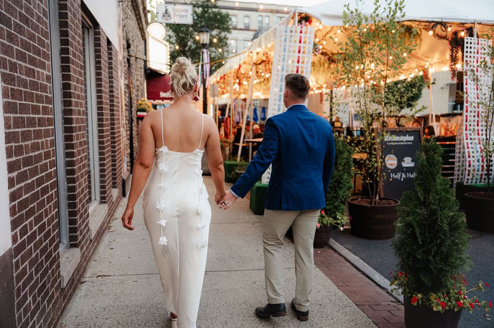 A bride in a white dress walks down a brick-lined pathway during an outdoor wedding ceremony.