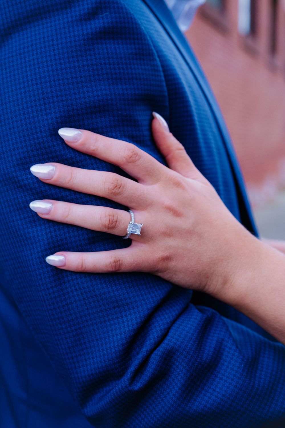 Close-up shots of an engagement ring with a sparkling diamond on a hand resting against a navy blue suit.